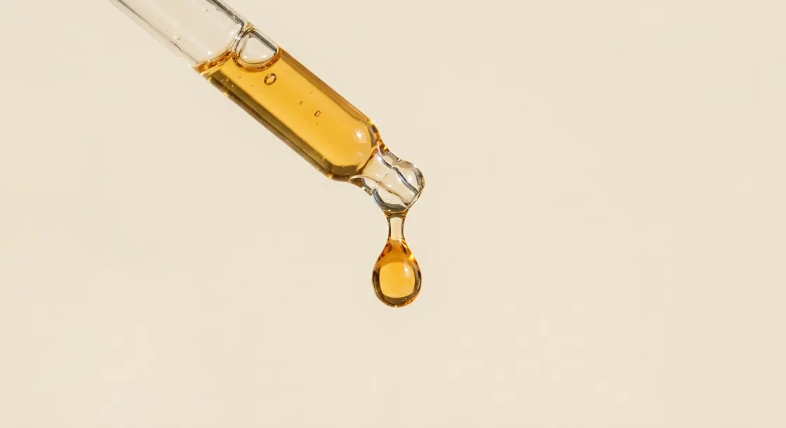 A single amber oil droplet forming at the tip of a glass dropper